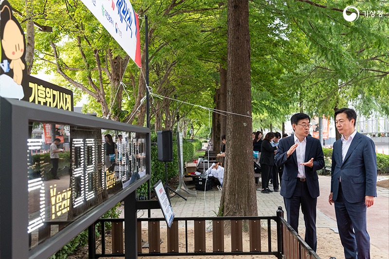 장동언 기상청 차장과 이택구 대전광역시 행정부시장이 기후변화시계 앞에서 대화를 나누는 사진;